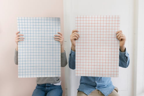 Two people holding grid paper posters in blue, one orange side by side