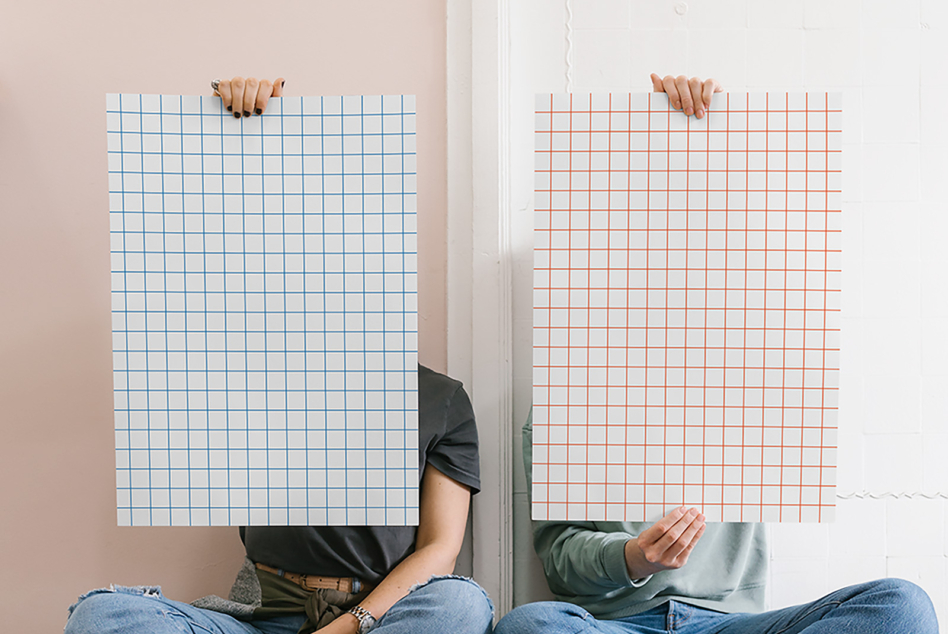 Two people holding large vertical grid papers with blue, orange lines