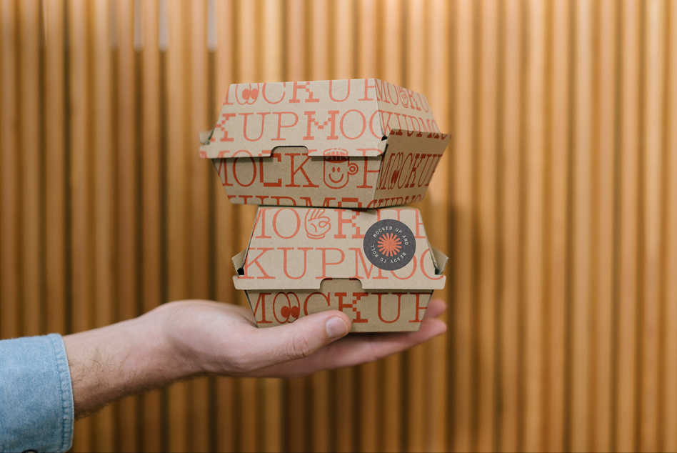 Hand holding stacked takeout boxes with orange branding mockup