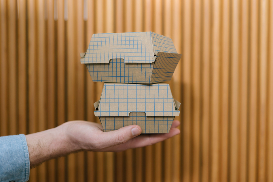 Hand holding stacked burger boxes with blue grid pattern mockup