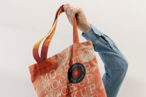 Hand holding coral orange tote bag with circular badge detail