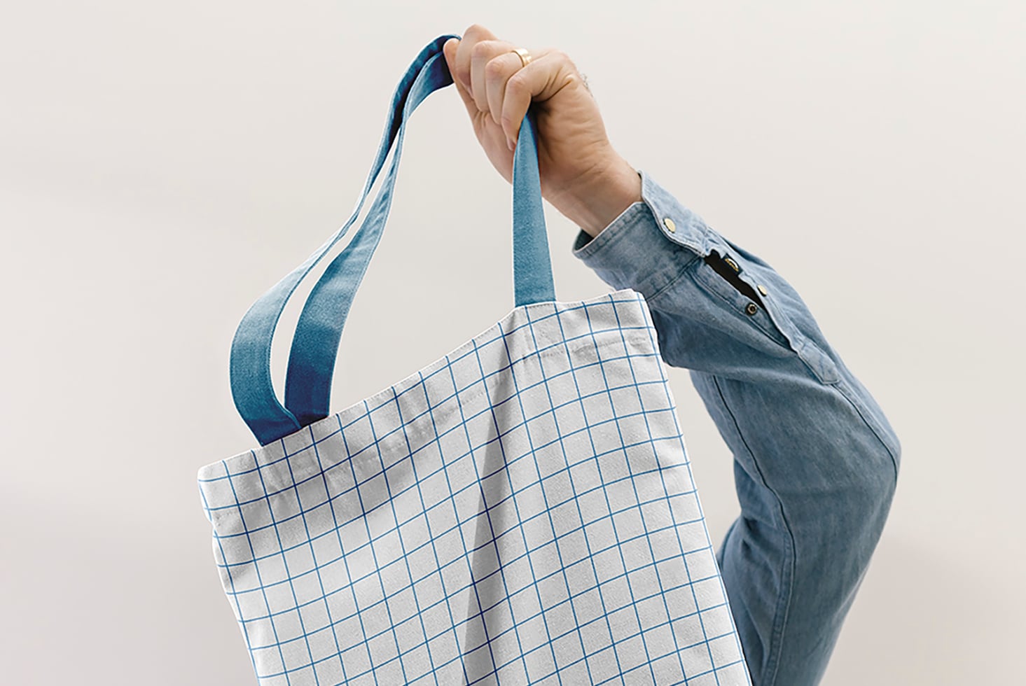 Hand holding blue grid canvas tote with denim jacket visible
