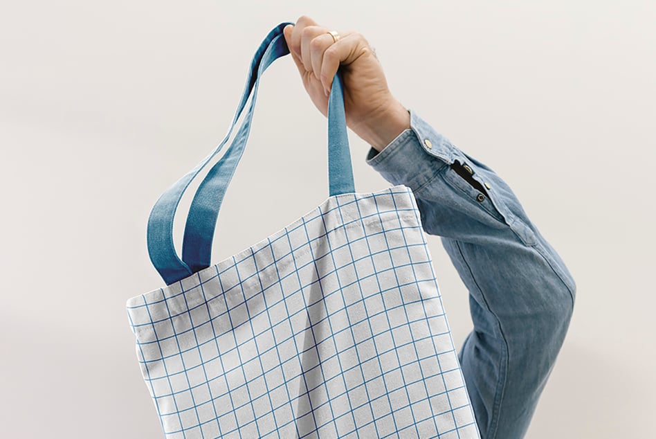 Hand holding blue grid canvas tote with denim jacket visible