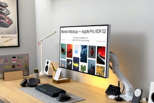 Desk setup with monitor mockup displaying portfolio, sticker-covered laptop visible