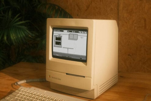 Vintage Macintosh Classic computer on wooden desk with potted plant beside it