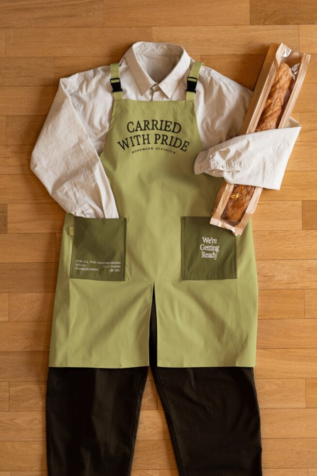 Lime green apron with black straps shown flat lay with cream shirt styled
