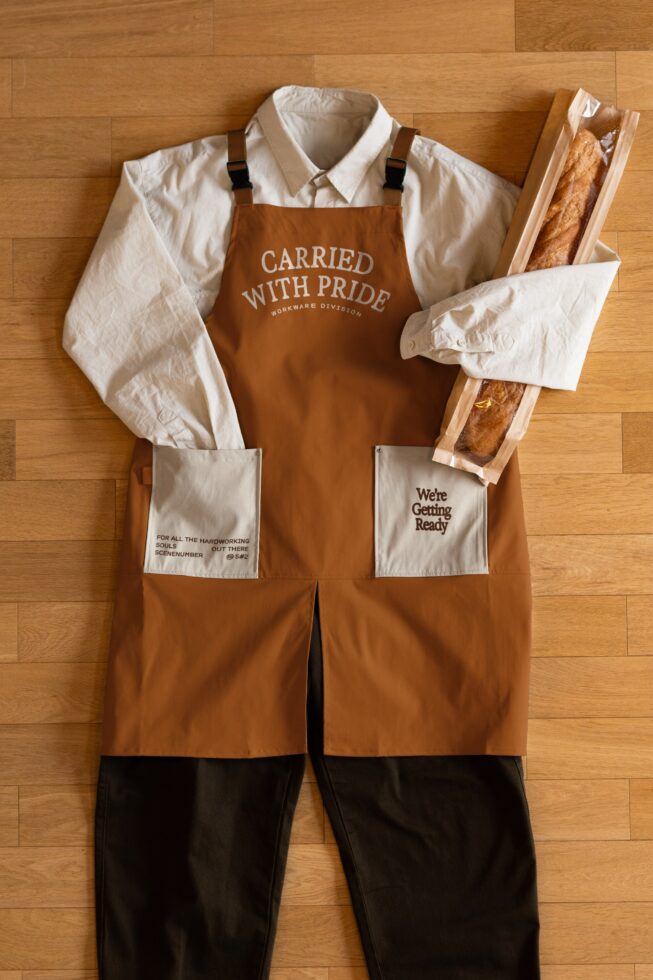 Rust apron with cream shirt styled flat lay with bread bags on wood