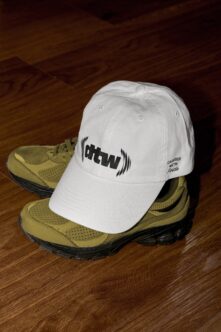 White cap with ohtwn logo on tan hiking boots wooden floor