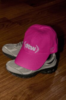 Bright magenta pink cap with white atw sound wave logo worn on sneaker display setup