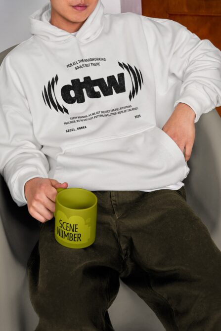White hoodie mockup with black graphic, holding yellow mug