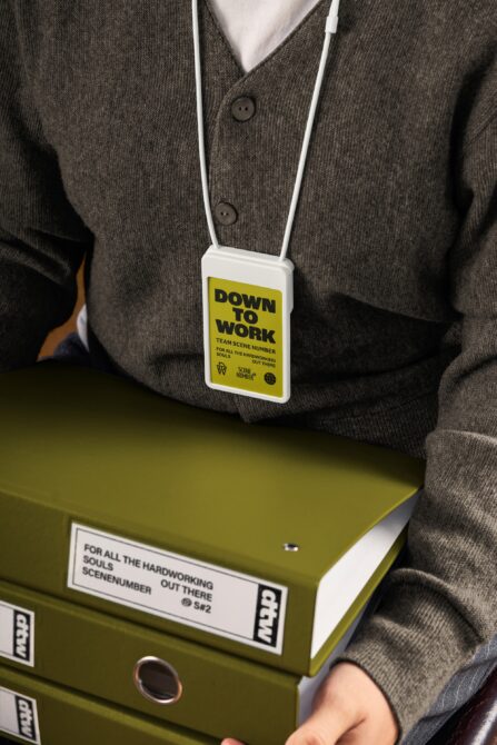 Yellow ID badge with Down to Work text worn on white cord over brown cardigan