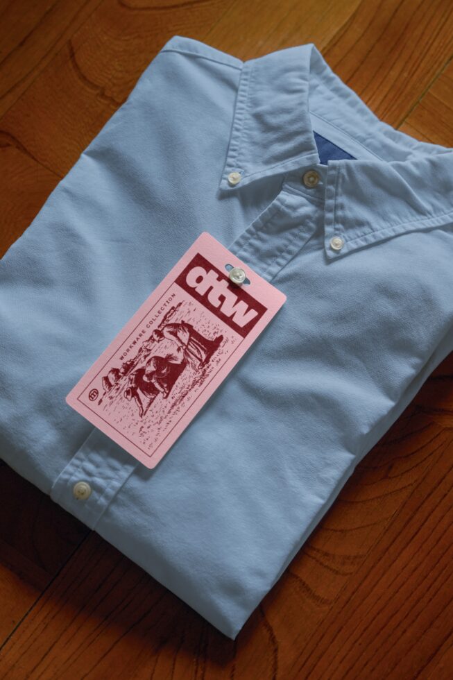Light blue button-up shirt with pink hang tag mockup on wooden surface