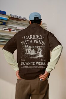 Color block brown plus cream jacket back featuring 'Carried with pride' engraving worn with light blue cap over shelving backdrop