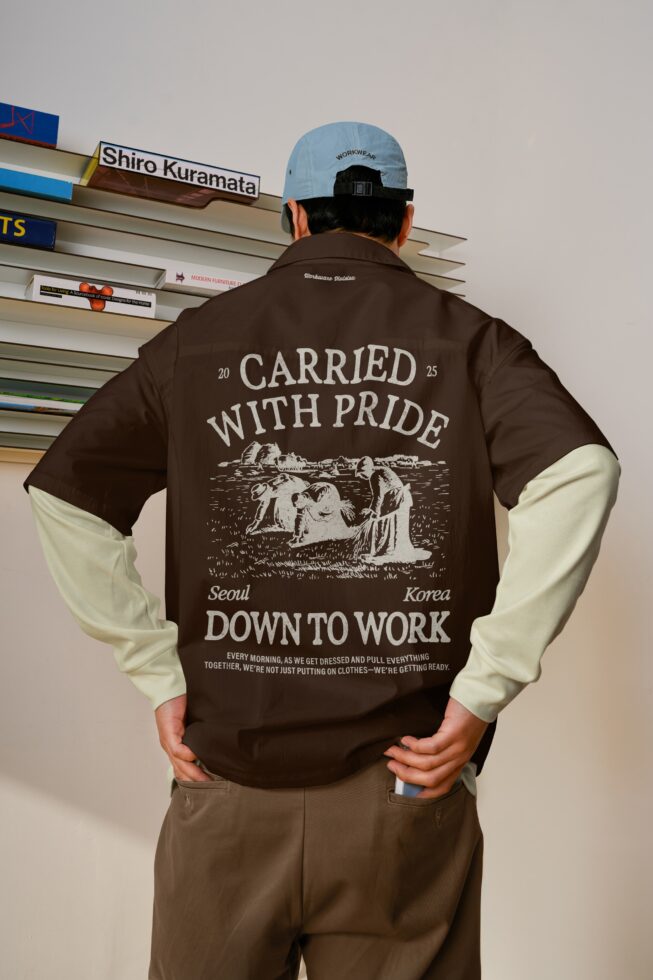 Color block brown plus cream jacket back featuring 'Carried with pride' engraving worn with light blue cap over shelving backdrop
