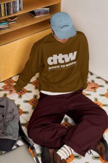 Guy in olive workwear sweatshirt, light blue cap, burgundy pants sitting down