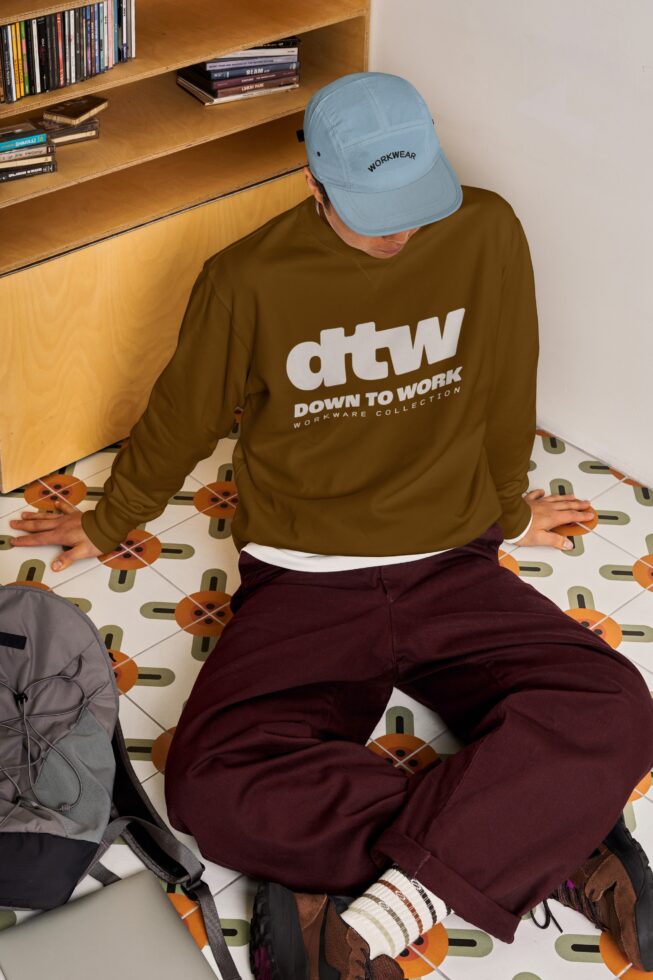 Guy in olive workwear sweatshirt, light blue cap, burgundy pants sitting down