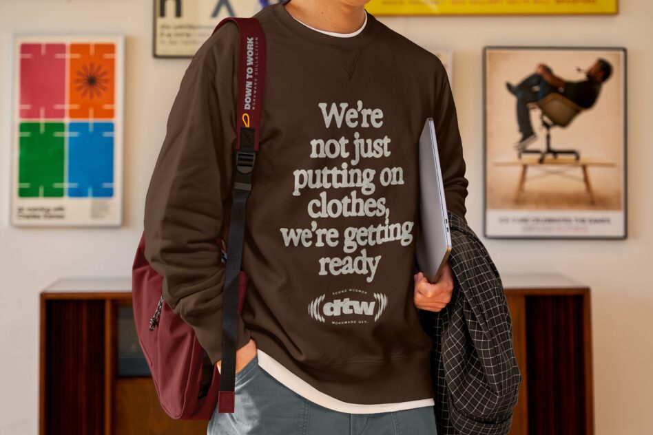 Full body shot of model wearing brown sweatshirt with burgundy bag in styled office setting