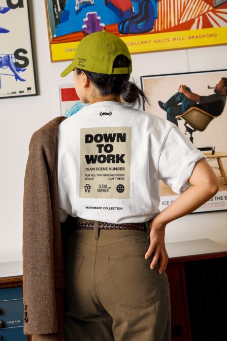 White tee with beige back print reading Down To Work over cream colored square patch
