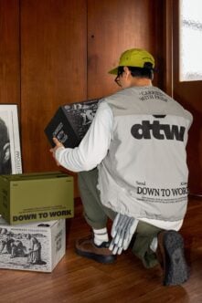 Worker in yellow hard hat holding black book box in beige jacket with dark text