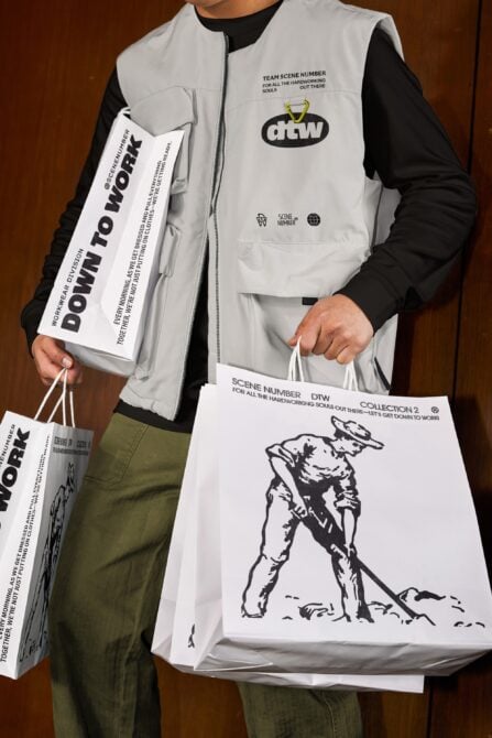 Beige puffer vest layered with black long sleeve, holding branded paper bags shown on model