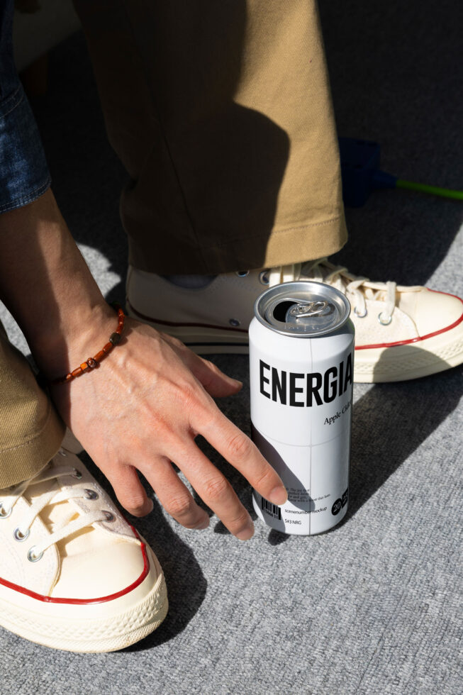 White Energia can being held near foot wearing beaded amber bracelet close-up