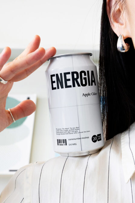 Woman in striped shirt holding white Energia apple cider can with ocean backdrop