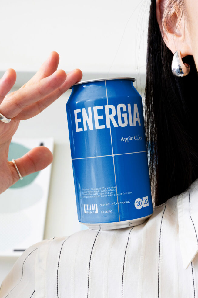 Woman holding blue Energia apple cider can by the ocean with drop earring visible