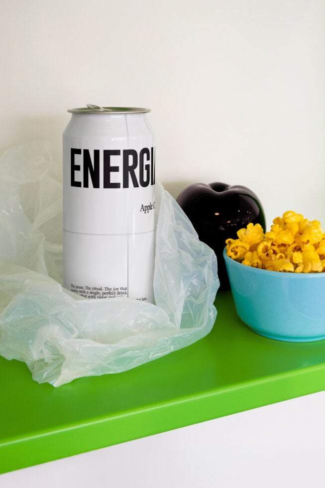 White energy drink can next to bowl of yellow popcorn on bright green surface