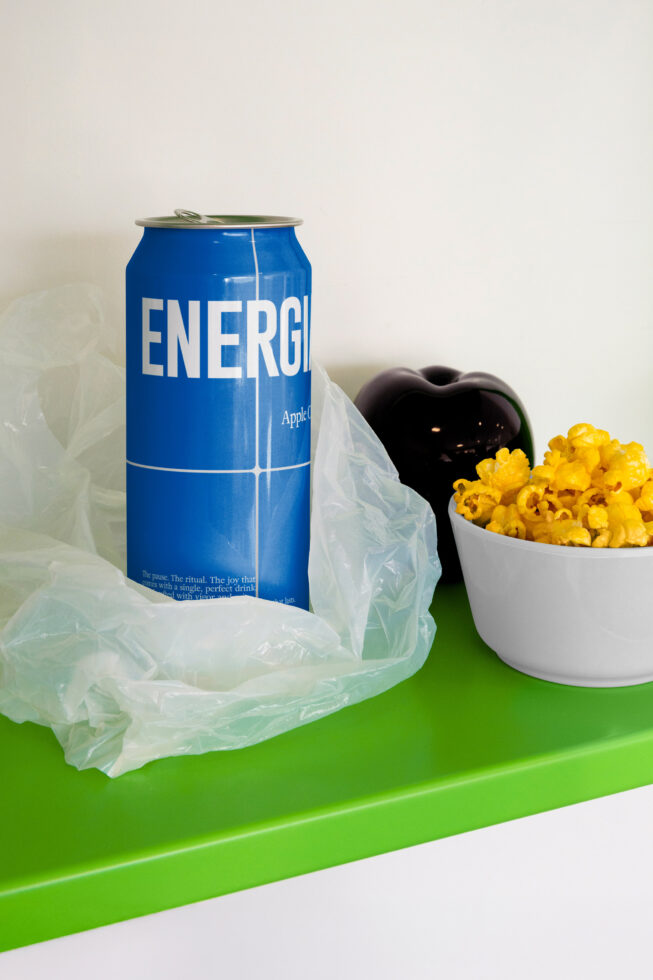 Blue ENERGIA can sitting on green shelf next to popcorn in white bowl with plastic bag