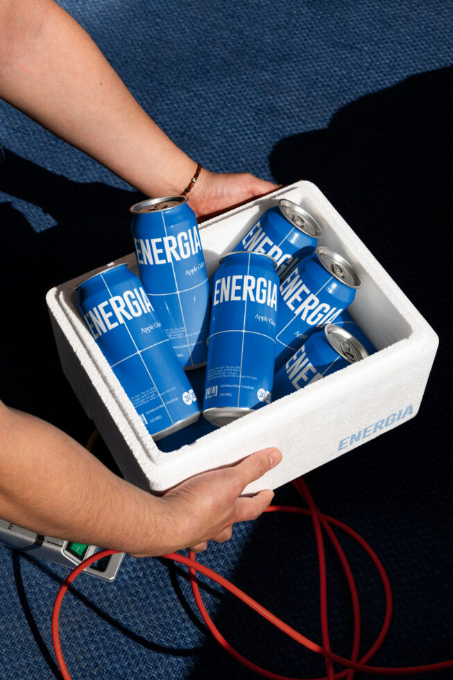 Blue cans in foam cooler being held up showing metallic finish in natural lighting