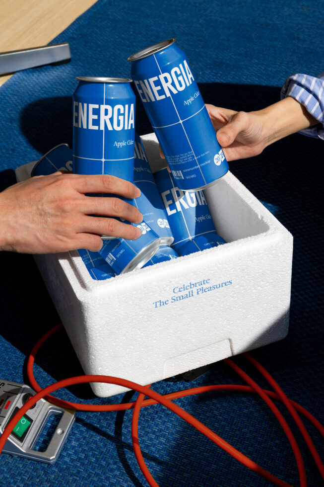 Two bright blue cans being pulled from white foam cooler on textured blue surface