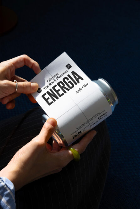 Hands holding white aluminum can with bold black ENERGIA lettering against dark background