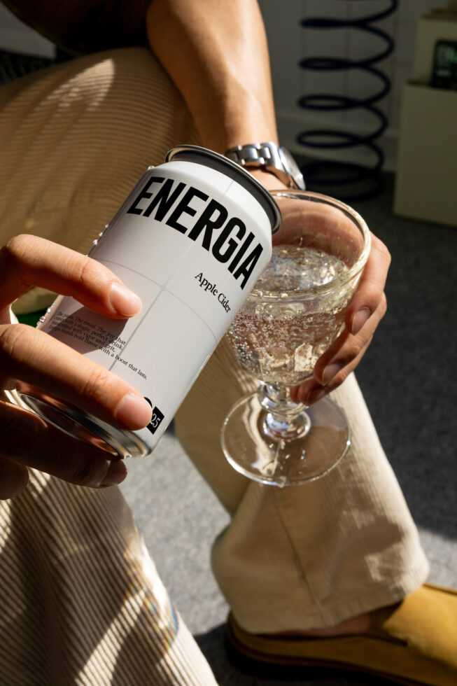 Hand holding white energy drink can next to clear glass with sparkling beverage, bright sunlight