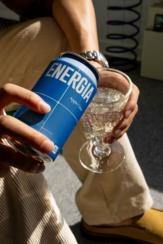 Blue aluminum can held beside filled glass beverage on soft neutral background