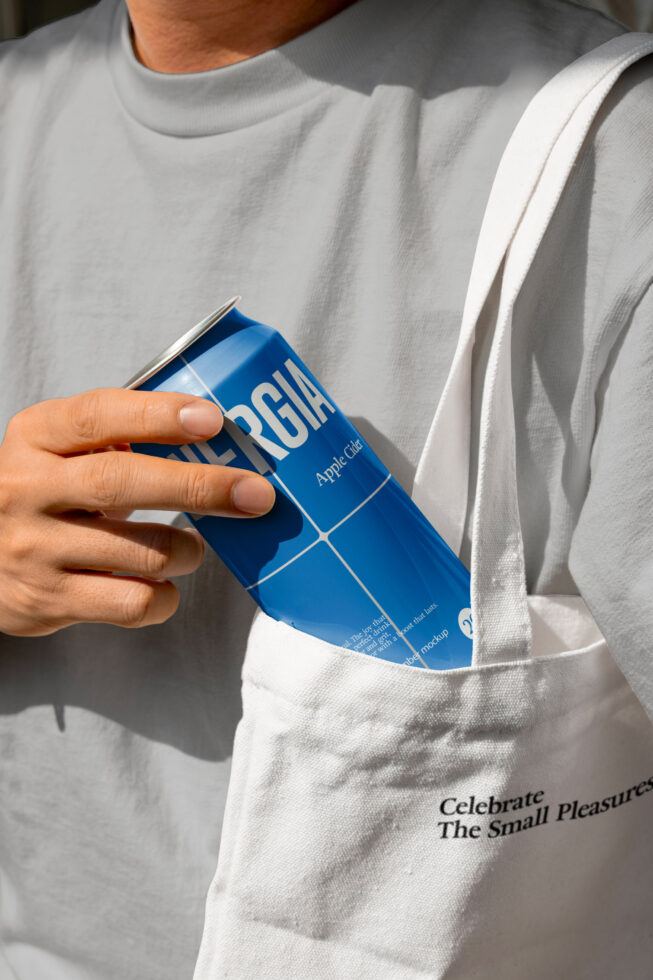 Person in cream tee holding blue beverage can in front pocket of white tote bag