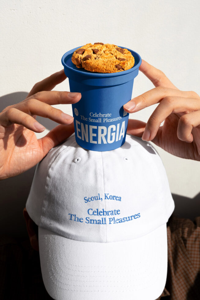 Hands holding blue cup with chocolate chip cookies, white cap with brand text
