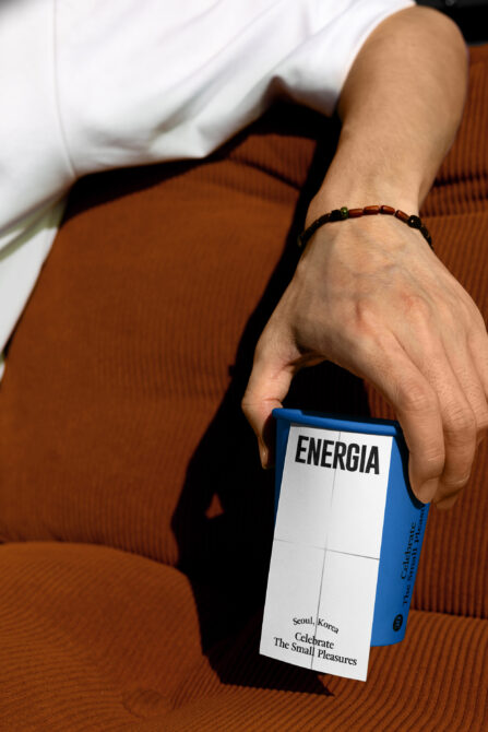 Hand holding paper cup mockup with blue Energia label on rust colored chair