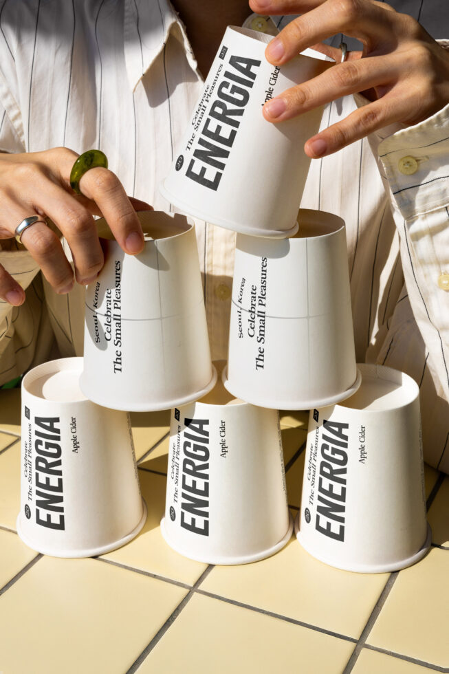 Multiple white paper cups with Energia branding, person pouring white cup into beige cup
