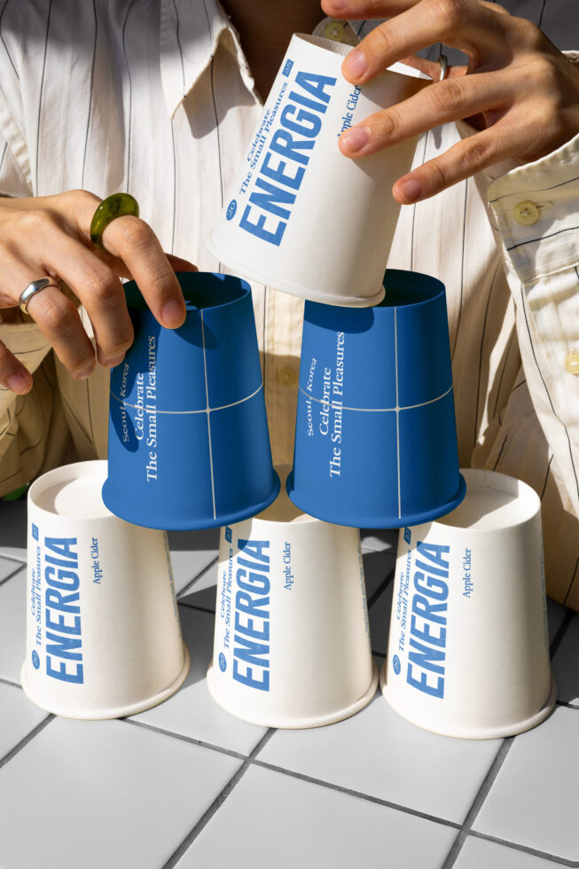 Hands pouring white paper cup into blue cup, multiple cups with Energia branding displayed