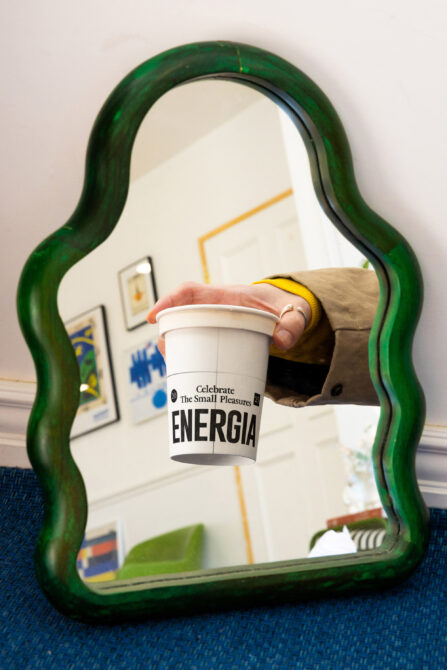 Green wavy mirror frame reflecting white Energia cup held in yellow sleeve