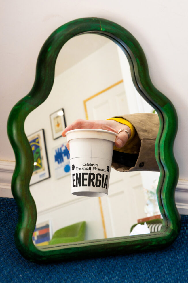 Green wavy mirror frame reflecting white Energia cup held in yellow sleeve