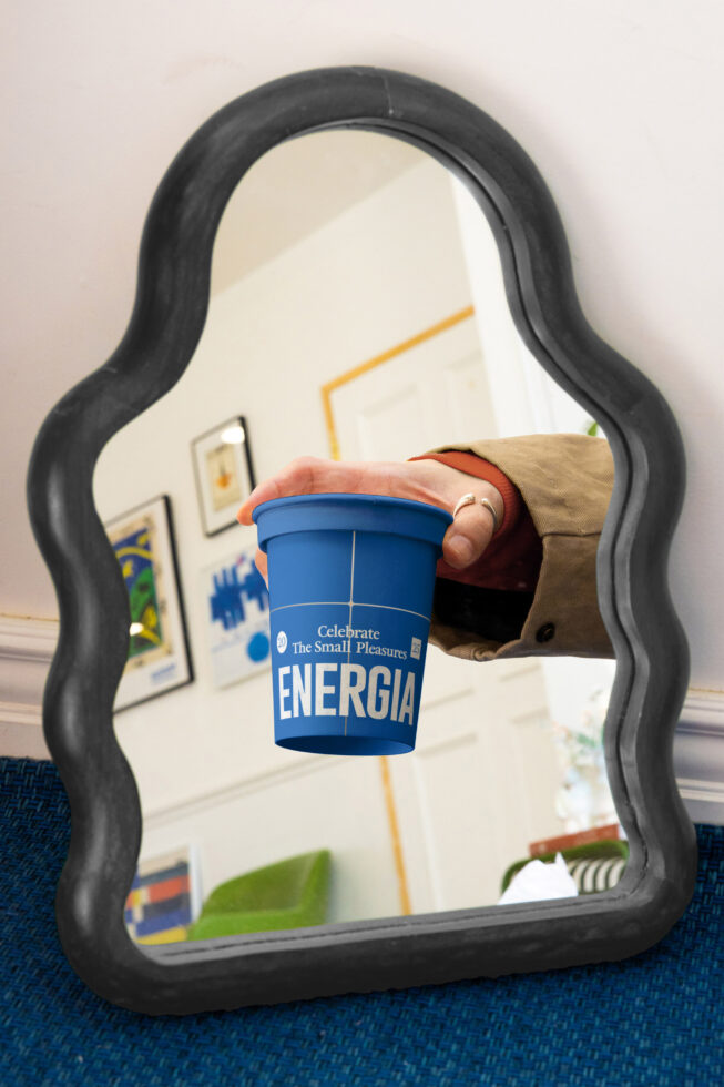 Black wavy mirror frame reflecting blue Energia cup held in brown sleeve