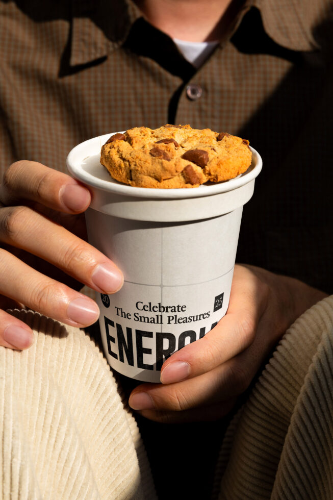 Hand holding paper cup with chocolate chip cookies, white label says Energia