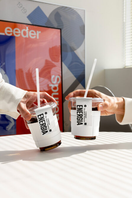 Two white beverage cups with dark text labels held in hands side by side