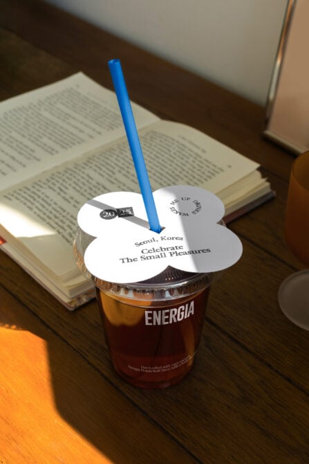 White flower-shaped drink lid with blue straw on Energia cup in desk setting