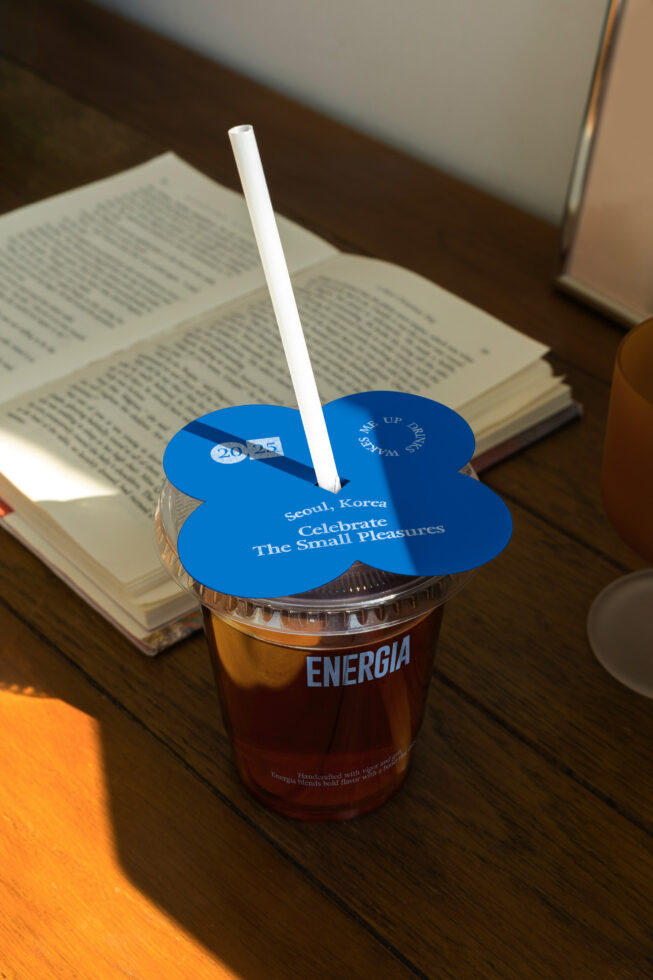 Blue flower-shaped drink lid with white straw on Energia cup in desk setting