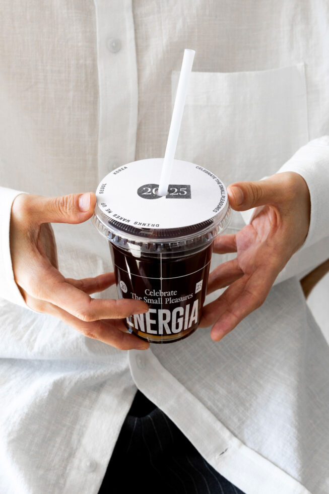 Hand holding iced drink with white lid showing date badge 20-25 celebration