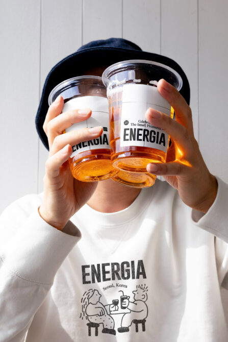 Person in white shirt with Energia print holding two clear jars with white label mockups