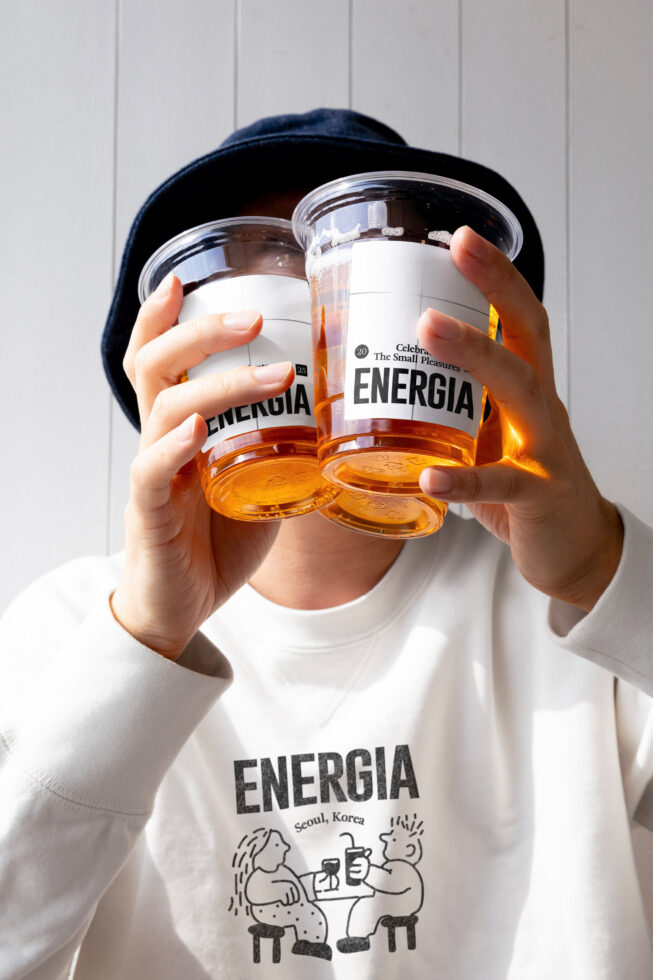 Person in white shirt with Energia print holding two clear jars with white label mockups
