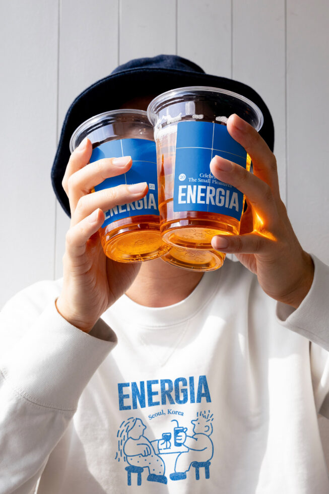 Person wearing white tee with blue Energia graphic, holding two jars with matching blue labels